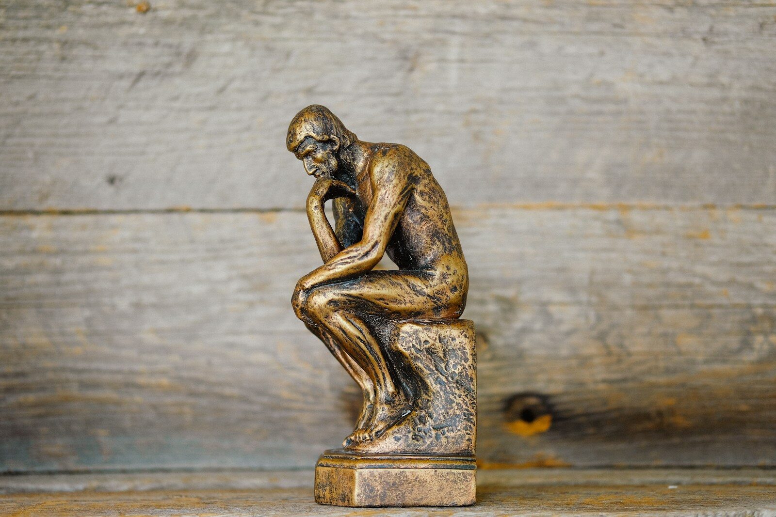 A bronze statue of a man in a pensive pose against a wooden background