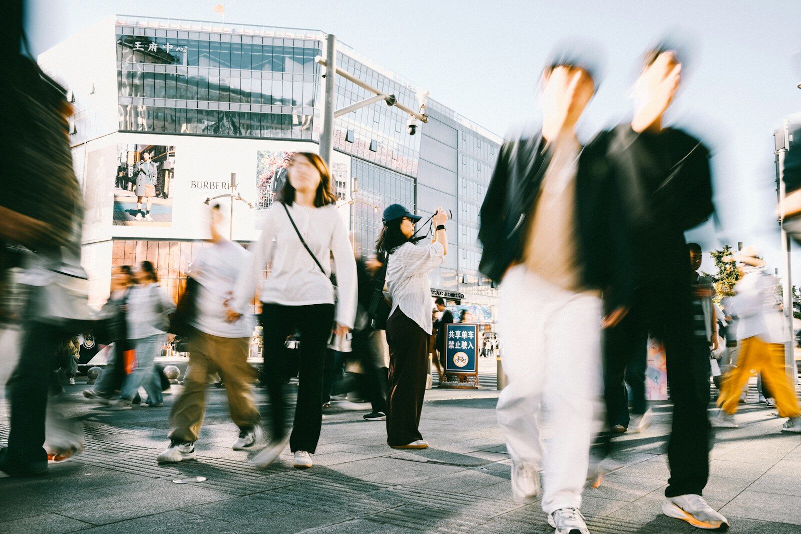 People walking through a busy city plaza with motion blur and a photographer
